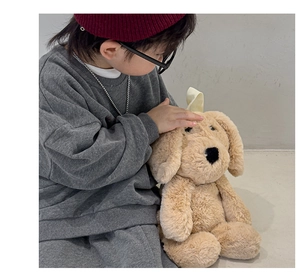 Detail shot of a toddler interacting with a beige plush puppy backpack for kids