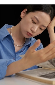 Detail of round white pearl necklace styled with a blue cotton shirt on a model