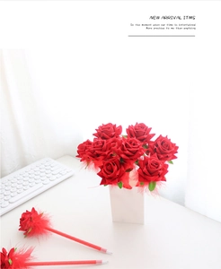 Close-up of elegant red rose flower ballpoint pens with feathers on a white desk