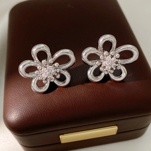 Macro detail of silver flower earrings with zircon center on leather texture background