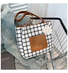 Detail of plaid tote bag featuring brown leather pocket and cute white cat charm accessory