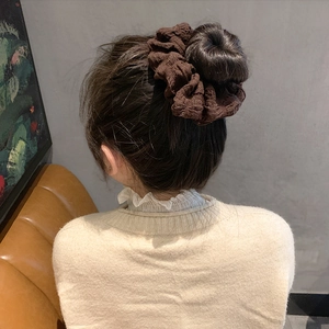 Brown textured scrunchie made of pleated fabric shown on an elegant hair bun