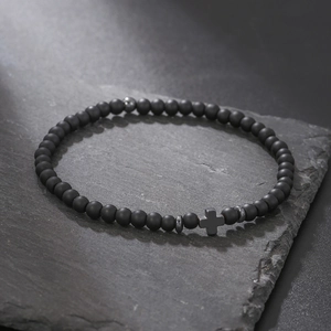 Macro shot of matte black hematite beads and metal cross charm on a dark stone surface
