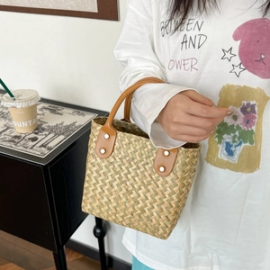 Detailed shot of woven straw handbag featuring brown leather handles and metal rivets