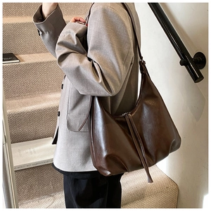 Deep brown oversized slouchy leather shoulder bag worn by model on stairs in soft lighting