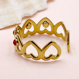 Macro shot of gold heart-shaped chain ring with red gemstones on a shell base