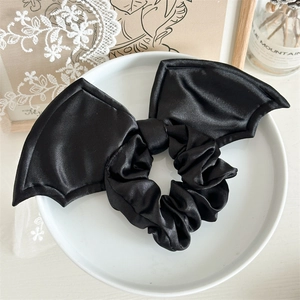 Detailed view of a black satin Halloween bat wing scrunchie on a white ceramic plate