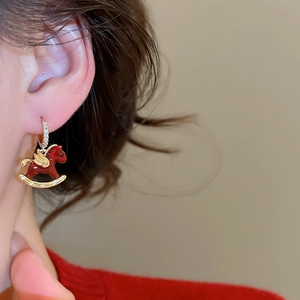 Détail de boucles d'oreilles cheval en émail rouge et zircons sur l'oreille
