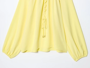 Detail van de felgele blouse met lange mouwen met vetersluiting en trekkoordje