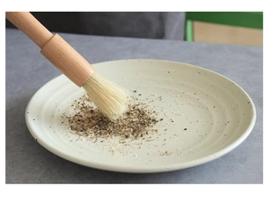 Détail d'un pinceau en hêtre à poils naturels appliquant des épices sur une assiette