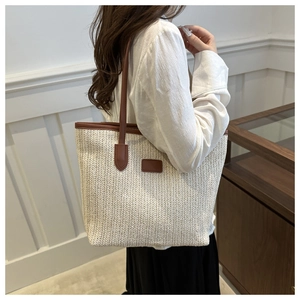 Detail of hand-woven straw tote bag featuring contrast brown leather straps and trim