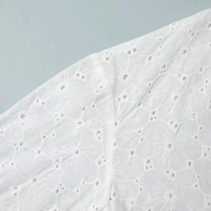Close-up of white summer dress showing detailed star-shaped eyelet embroidery and cotton fabric