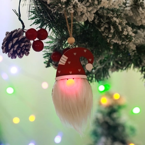 Close-up of a glowing Christmas gnome ornament with red hat on a snowy pine branch