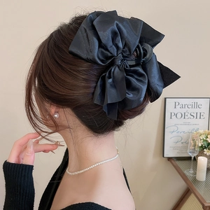 Detail showing an elegant large black satin bow hair claw clip worn on a woman's hair
