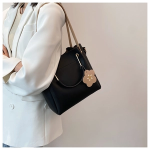 Detailansicht der schwarzen Beuteltasche mit Blumenanhänger an Model in weißem Blazer
