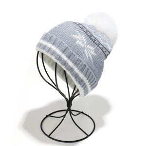 Close-up of winter knit hat in light blue with white snowflake patterns and a fluffy faux fur pom