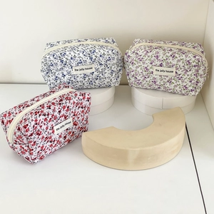 Close-up of floral fabric pouches with zipper and woven labels in minimalist white setting