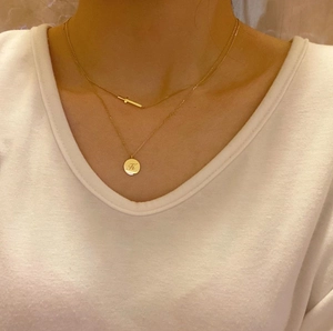 Close-up of a layered gold 925 silver necklace with a horizontal bar and K-letter pendant