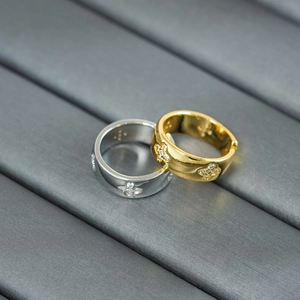 Close-up of gold and silver four-leaf clover rings with white zircon stones on grey surface