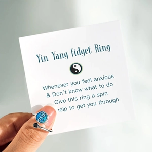 Detail of Yin Yang fidget ring with blue enamel and crystal on an informative card