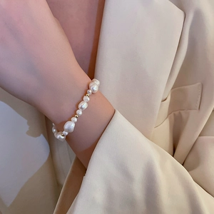 Close-up of baroque pearl bracelet with gold beads worn on a beige blazer sleeve