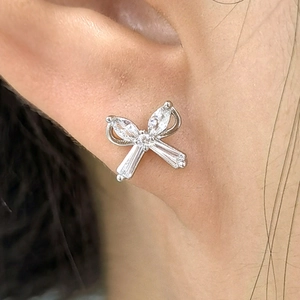 Macro shot of silver bow stud earrings with zircon stones worn on the earlobe