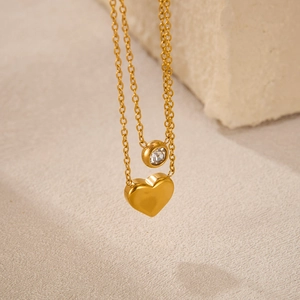 Detail of gold double-layered heart necklace with zircon pendant on a stone background