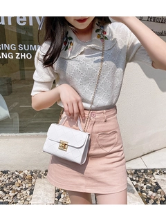 Detail of white quilted crossbody bag with gold chain strap and turn-lock closure on model