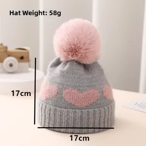 Detailed view of baby knitted beanie with heart pattern, pink faux fur pom and 17x17cm dimensions