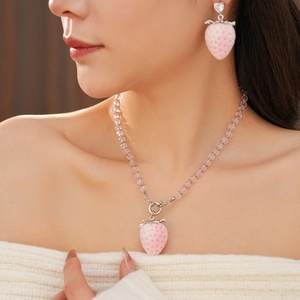 Macro shot of pink strawberry pendant earrings and beaded necklace with heart gem
