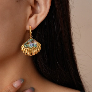 Close-up of a model wearing a gold shell earring featuring colorful abalone shell inlay