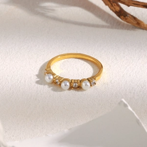 Close-up of gold ring with three white pearls and two clear zircons on stone surface