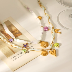 Détail du collier foulard en soie avec pendentifs coquillage et cœur dorés et perles violettes