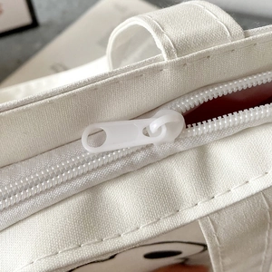 Detail view of smooth zipper, sturdy handle, and neat stitching on white canvas tote bag