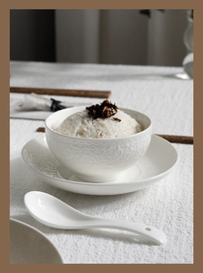 Detail of white embossed ceramic bowl and spoon set featuring elegant floral patterns
