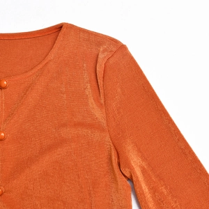 Détail du tricot côtelé orange avec boutons assortis sur un gilet court à manches longues
