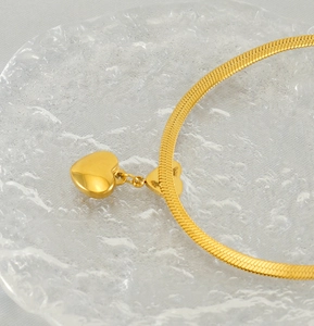 Détail d'un collier pendentif cœur doré sur une chaîne serpent plate sur verre