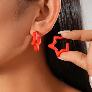 Detailed view of red matte star earrings on ear and held between fingers