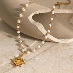 Dettaglio della collana di perle con ciondolo a sole su sfondo in pietra e luce calda