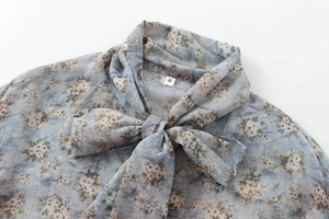 Détail du nœud au col d'un chemisier en mousseline gris-bleu avec imprimé floral