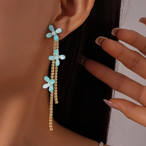 Detail view of light blue resin flower earrings with gold tassels and white pearls on model