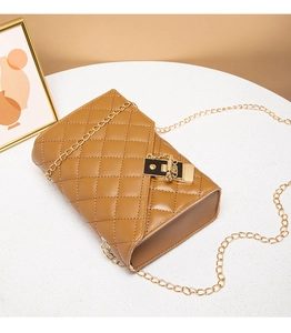 Detail of brown quilted PU leather shoulder bag with golden chain and black metal buckle