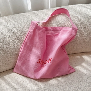 Detail of pink canvas tote bag with red letter print resting on a soft cream fleece sofa