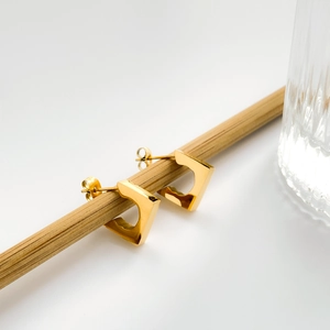 Detail of geometric D-shape gold hoop earrings hanging on a minimalist wood stand
