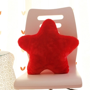 Modern red star-shaped plush pillow on a white chair with soft lighting and cozy setting