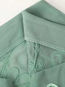 Détail du tissu brodé vert clair montrant les coutures et la texture de qualité