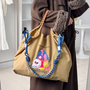 Detail of beige nylon tote bag featuring artistic embroidery and blue braided strap