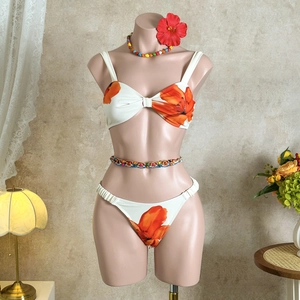 Detail of white bikini with orange floral print, twist front top and beaded accessories