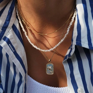 Layered gold necklace featuring a blue enamel dolphin pendant and elegant pearls