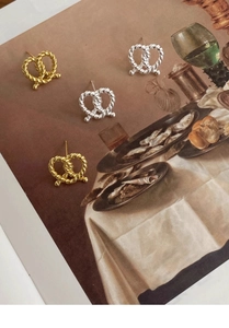 Artistic close-up of silver and gold twist knot earrings on vintage background
